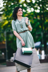 stylish brunette in tunic stands with glasses and with shopping in her hands in the park in the summer