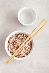 Assorted multi-colored wild rice in ceramic bowl and chopsticks with goblet of water. Black, brown and white rice...