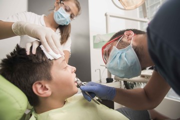 Fototapeta premium A boy having his tooth removed is being comforted by a nurse at the dentist office - oral hygiene health care concept