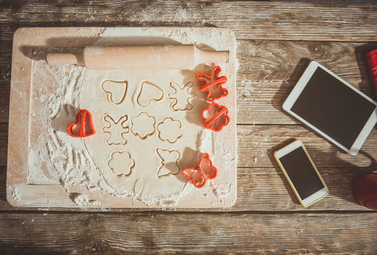 Unfinished cookies of different shapes on processing board. Gadgets, cutters and rolling pin are near. Close up top view