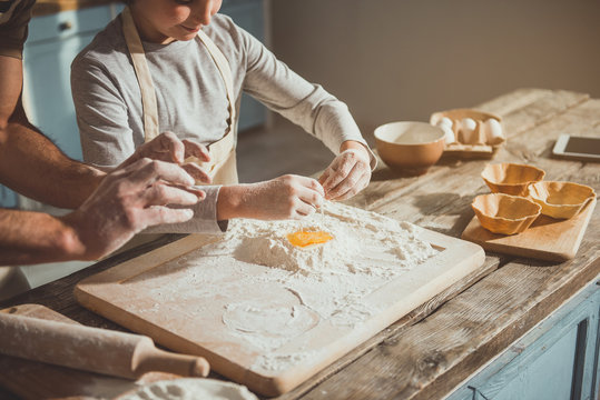 Dad teaching son smashing eggs. Boy pouring egg into the flour. Cooking implements on table