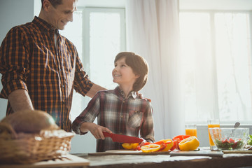 Man and boy standing in cooking room. Child slicing veggies while dad looking at him with proud....