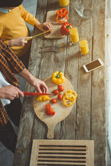 Top view of dad and kid cutting veggies for healthy salad on wooden table. Close up