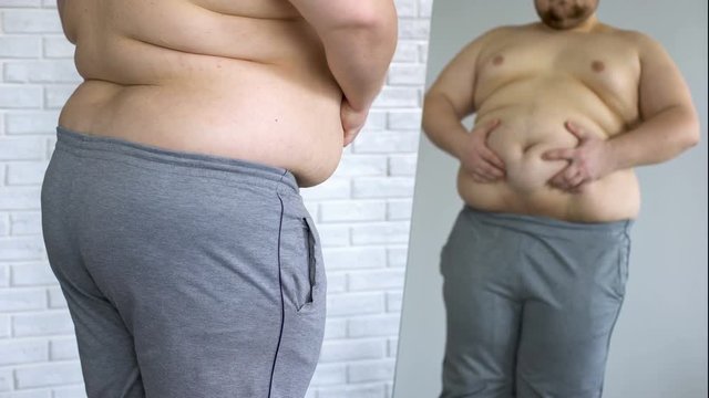 Sad overweight man looking at fat belly mirror reflection, weight loss problem