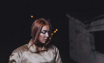 Abstract photo of a beautiful young woman in a beige silk coat against a background of concrete walls of an underground city station.