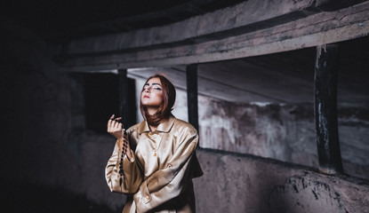 Fototapeta na wymiar Abstract photo of a beautiful young woman in a beige silk coat against a background of concrete walls of an underground city station with cherries in hand.