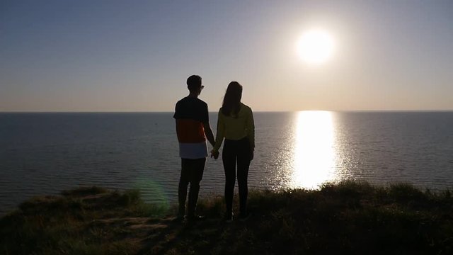 Back view with a zoom in of an amorous man with his nice girlfriend at a splendid sunset with a shining sun path at the Black Sea in slo-mo