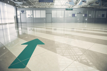 Big green arrow pointing at white closed door while locating on striped floor in airport hall