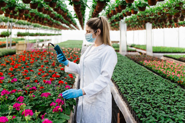 Beautiful young woman working at plant nursery and holding soil ph meter. 