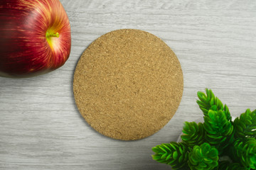 Cork board on light wood background with apple and potted plant.