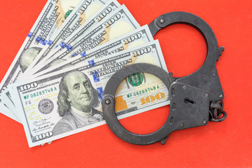 black metal handcuffs lying on the 100 dollars banknotes on a red background