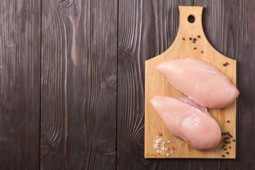 Recipe. Raw chicken breast with spices and salt on cutting board. Brown wooden background. Flat view. Copy space for text and design