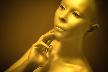 beautiful girl of unusual appearance, painted in gold paint. Holds his hand elegantly. sparkling beauty