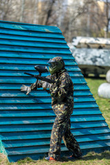 Boy in camouflage suit stands on the paintball field with his paintball gun up and looks straight ahead. team work, sport lifestyle