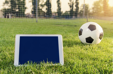 White tablet on grass field next to soccer ball, copy space, sports app concept 