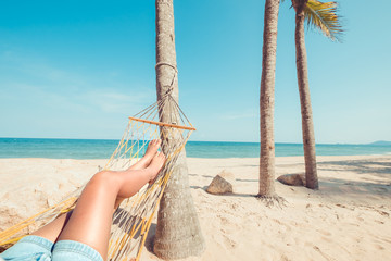Leisure in summer - Beautiful Tanned legs of sexy women. relax and sunbathe on hammock at sandy tropical beach. vintage color styles