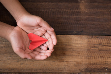 hand showing or holding red paper airplane on wooden table background. freedom and childhood concept