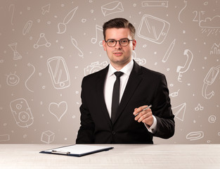 Young handsome businessman sitting at a desk with white mixed media icons behind him