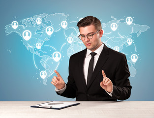 Young handsome businessman sitting at a desk with a blue world map behind him