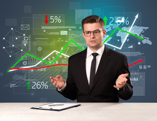 Young handsome businessman sitting at a desk with stocks and progress charts behind him