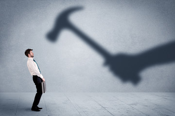 Business person afraid of a shadow hand holding hammer concept on background