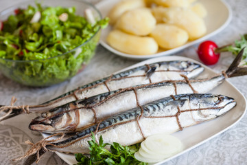Appetizingly served mackerel on a white table, together with a potato salad and greens