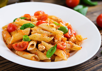 Penne pasta in tomato sauce with chicken, tomatoes, decorated with basil on a wooden table. Italian food. Pasta Bolognese.