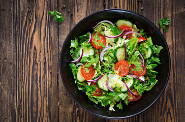 Salad from tomatoes, cucumber, red onions and lettuce leaves. Healthy summer vitamin menu. Vegan vegetable food. Vegetarian dinner table. Top view. Flat lay
