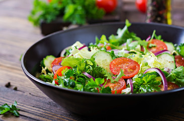Salad from tomatoes, cucumber, red onions and lettuce leaves. Healthy summer vitamin menu. Vegan vegetable food. Vegetarian dinner table.