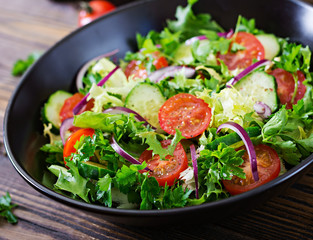 Salad from tomatoes, cucumber, red onions and lettuce leaves. Healthy summer vitamin menu. Vegan vegetable food. Vegetarian dinner table.