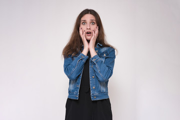 Portrait of a beautiful brunette girl on a gray background showing surprise in a jeans.