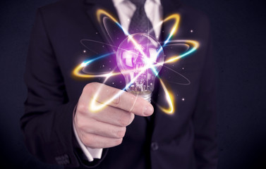 A classy businessman holding a colorful light bulb with shining circles in front of dark background concept.