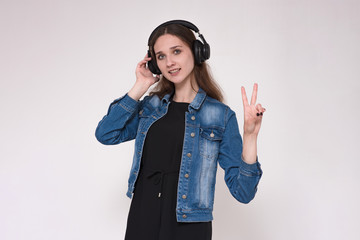 Portrait of a beautiful brunette girl on a gray background listening to music in headphones with a smartphone in a jeans