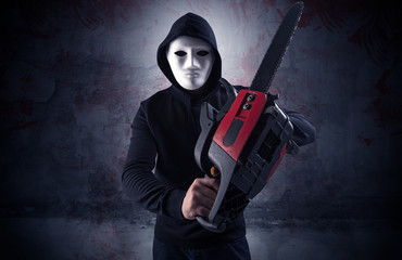 Armed rude assassin in an empty bloody room concept with gun ax chainsaw mallet wrench
