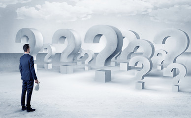 Fototapeta premium Businessman standing and looking to a bunch of question mark signs 