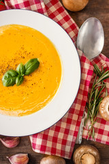 Squash Soup with herbs. Cream soup with  Pumpkin and Carrot  on Red classic Checkered tablecloth on wooden rustic table. Top view. Copy space.