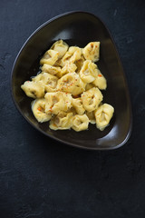 Tortellini in bouillon served in a black bowl, high angle view over black stone background, vertical shot