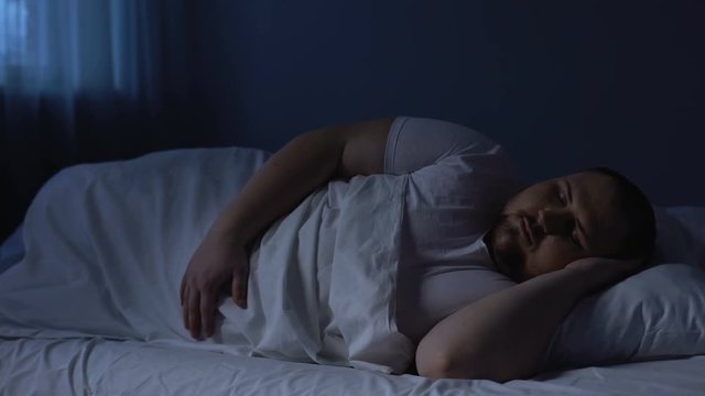 Plump man sleeping in bed, relaxing at night on comfortable mattress, rest