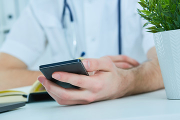 Close up male doctor or medical student using mobile smart phone working on laptop computer in hospital.