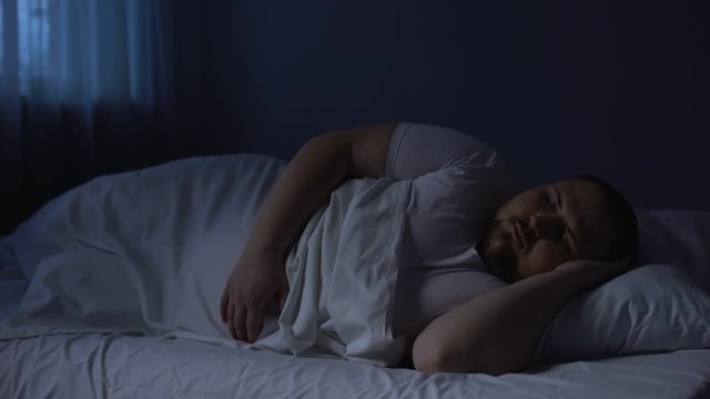 Obese man tossing in bed at night, sleeping disorder, insomnia disease, apnea