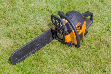 Naklejka premium Black and orange chainsaw on grass