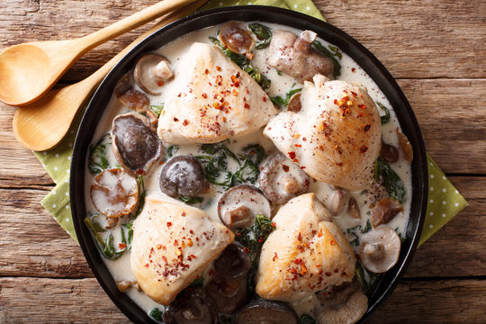 Pieces of chicken with wild mushrooms and spinach in a creamy sauce close-up on a table. horizontal top view