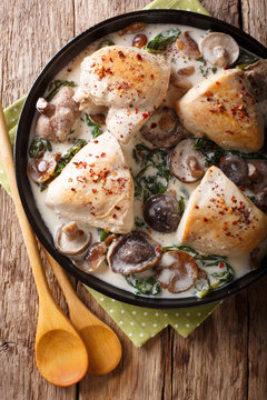 Pieces of chicken with wild mushrooms and spinach in a creamy sauce close-up on a table. Vertical top view