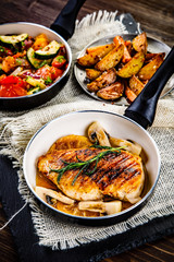 Roast chicken breast with potatoes and vegetables on wooden background