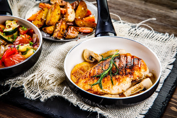 Roast chicken breast with potatoes and vegetables on wooden background