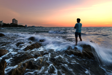 The man on the rocks at the sea with sunset sky