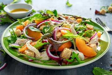 Fresh salad with chicken breast, peach, red onion, croutons and vegetables in a green plate....