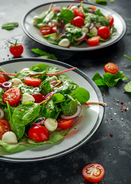 Fresh Cherry Tomato, Mozzarella salad with green lettuce mix and red onion. served on plate. healthy food.