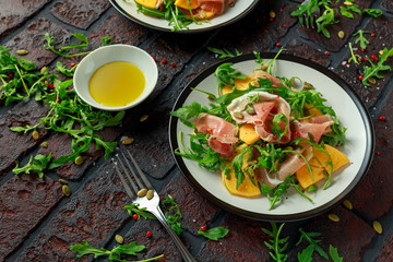 Fresh Tasty Persimmon salad with arugula, parma ham, olive oil, pumpkin seeds and herbs. autumn, winter healthy food