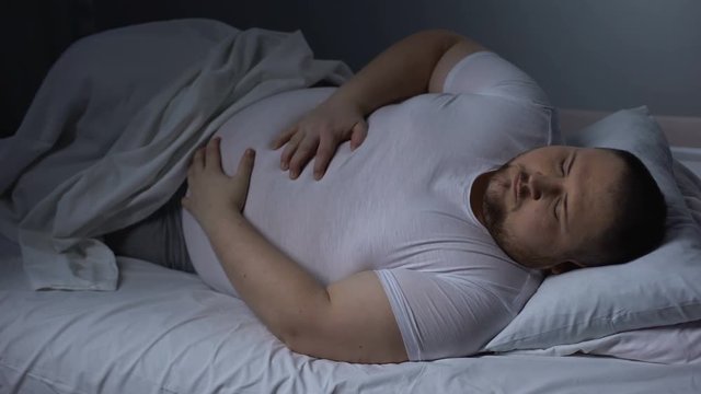 Fat man suffering from stomach pain at night, health problem, ulcer discomfort